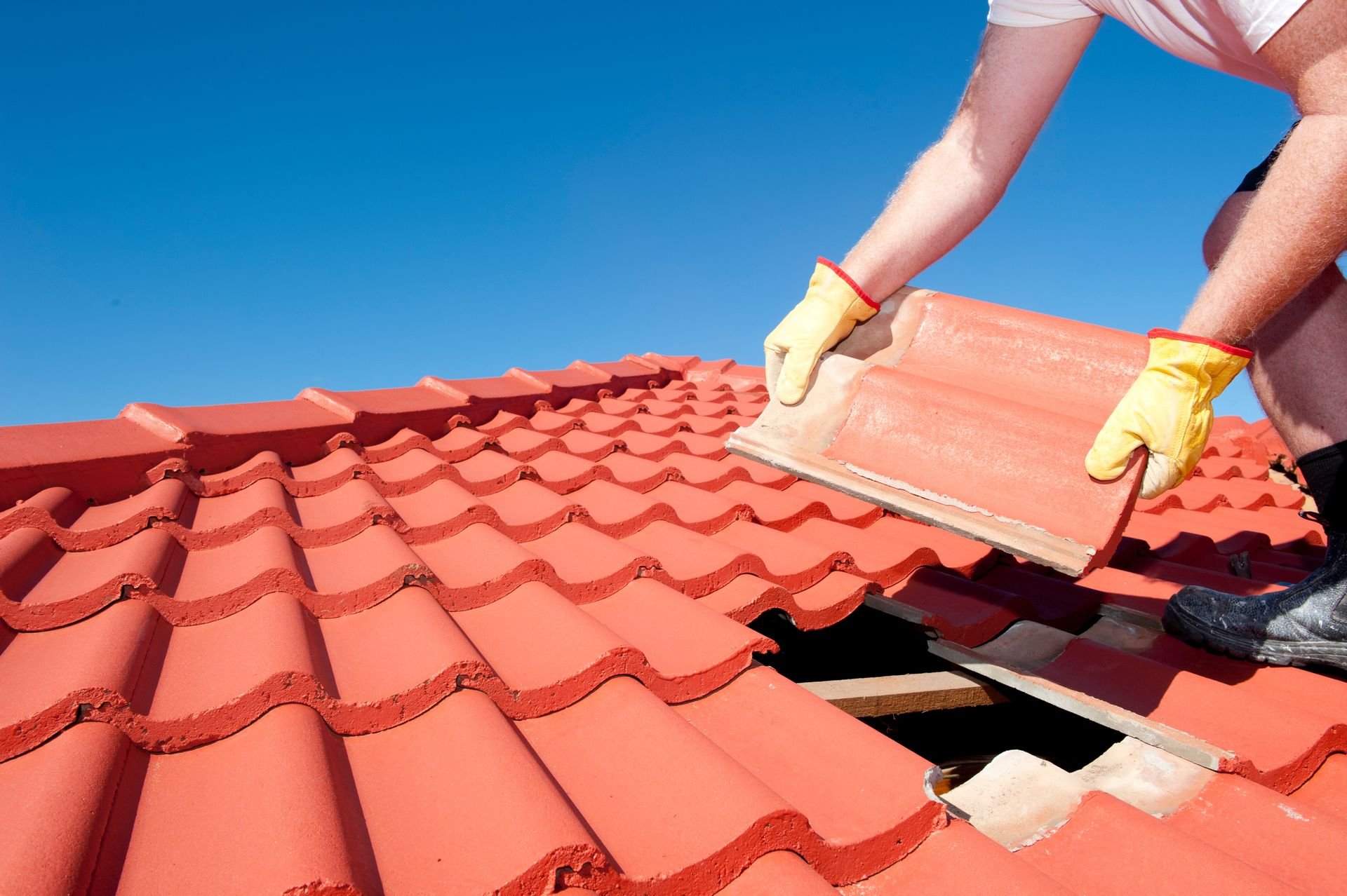 A roofer installing terracotta roof tiles on a bright sunny day