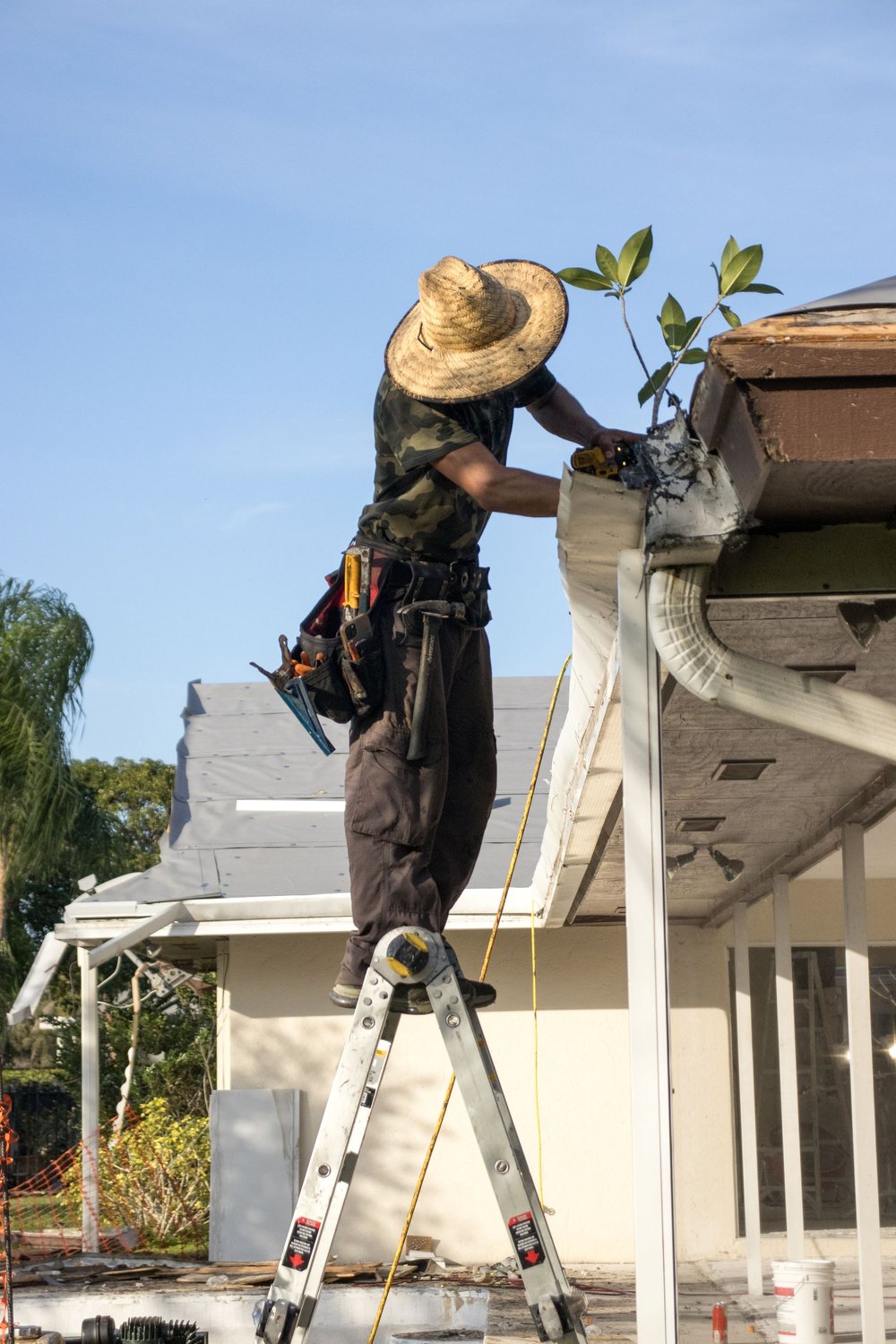 A technician on a ladder repairing a gutter and roofline