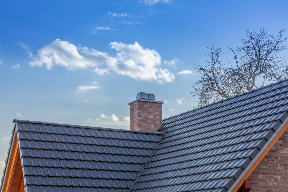 A brick chimney between gabled sections of a dark-tiled roof